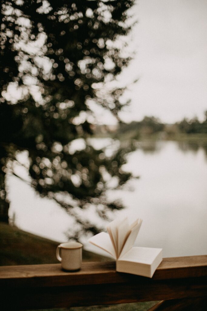 Ein aufgeschlagenes Buch und eine Tasse an einem ruhigen See