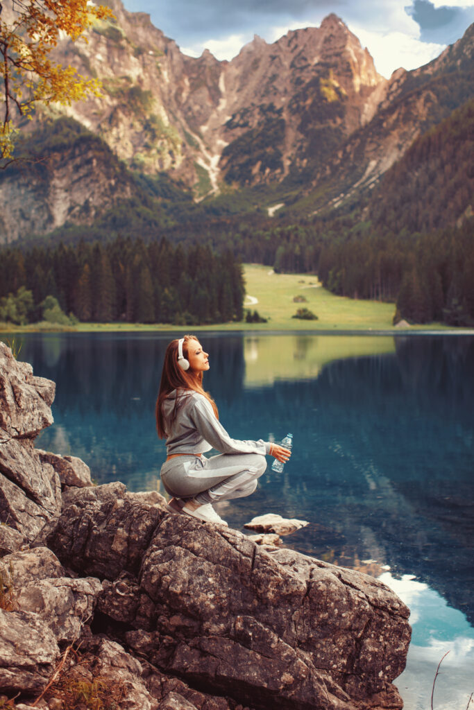 Frau sitzt mit einer Wasserflasche an einem Bergsee