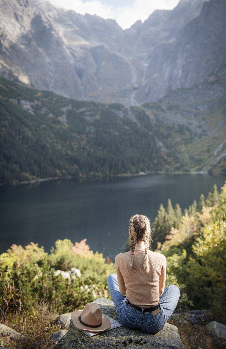 Frau blickt von einem Felsen auf einen stillen Bergsee